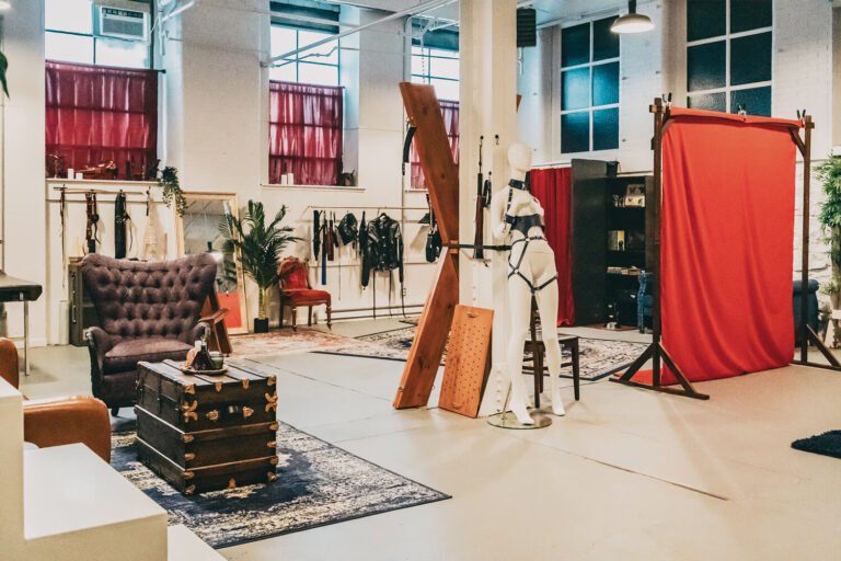 Wide view of the Cincinnati Ohio BDSM dungeon of professional dominatrix, Countess Cecilia. The large, open space contains a St. Andrew's cross, a spanking bench, and bondage table, and various whips, floggers, bondage straps, and more. A red backdrop on a wooden stand rest in front of the velvet couch to be used for custom fetish content.