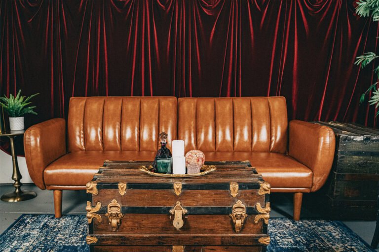 A luxurious red velvet curtain draped behind a leather couch and vintage steam trunk with a crystal skull and candles on top sit in the Cincinnati Ohio BDSM dungeon of professional dominatrix, Countess Cecilia.