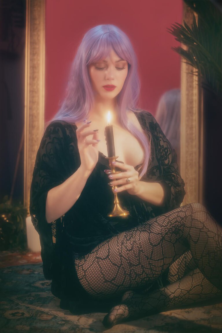 Cincinnati dominatrix and fetish model Countess Cecilia is dressed as a witch with long purple hair and black lace gown with fishnet pantyhose sits in front of the mirror while teasing the flame of a candle with her hand for this custom fetish content photoshoot.