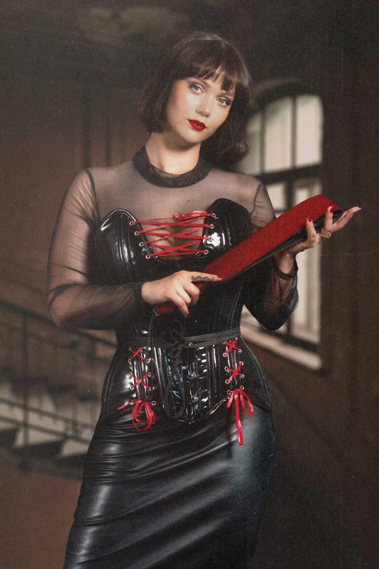 Cincinnati dominatrix, Countess Cecilia, stands outside of her BDSM dungeon, wearing a black corset gives a demanding look as she holds a thick leather flogger in her hand, preparing for an impact play session.